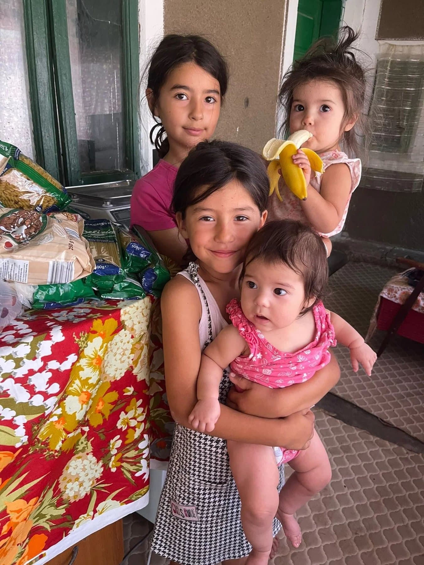 Children smiling together, the youngest holding a banana